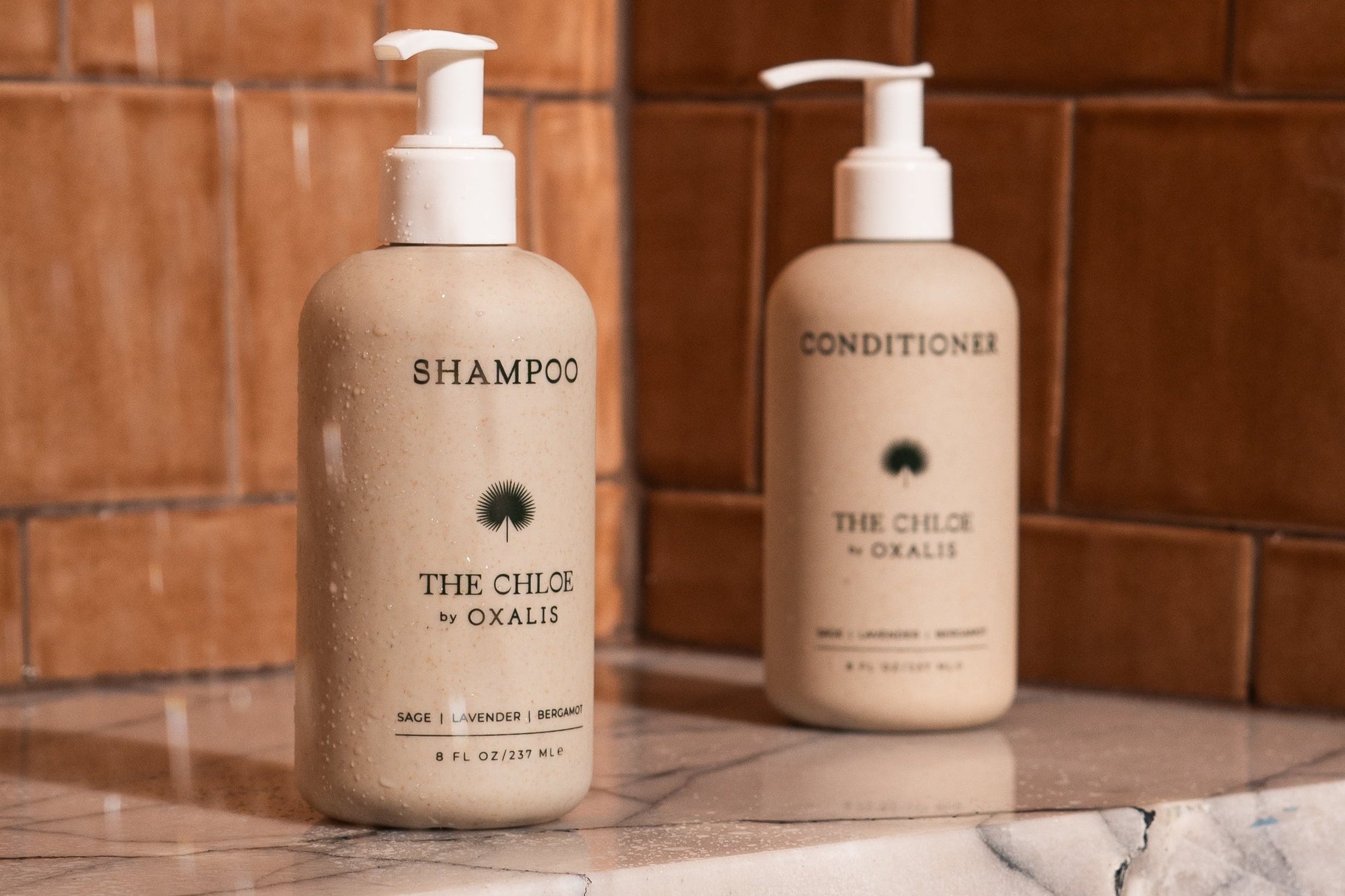 Shampoo and conditioner bottles labeled 'The Chloé by Oxalis' on a tiled bathroom counter.