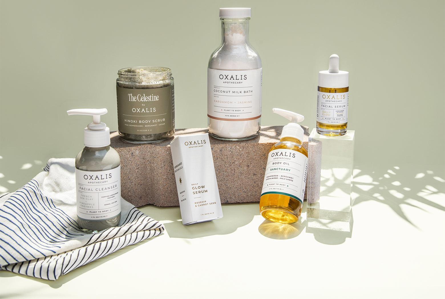 Oxalis Apothecary plant-powered skincare collection featuring French Sea Clay Facial Cleanser, Hinoki Body Scrub, Coconut Milk Bath, Daily Glow Facial Serum, and Sanctuary Body Oil, handcrafted in New Orleans.