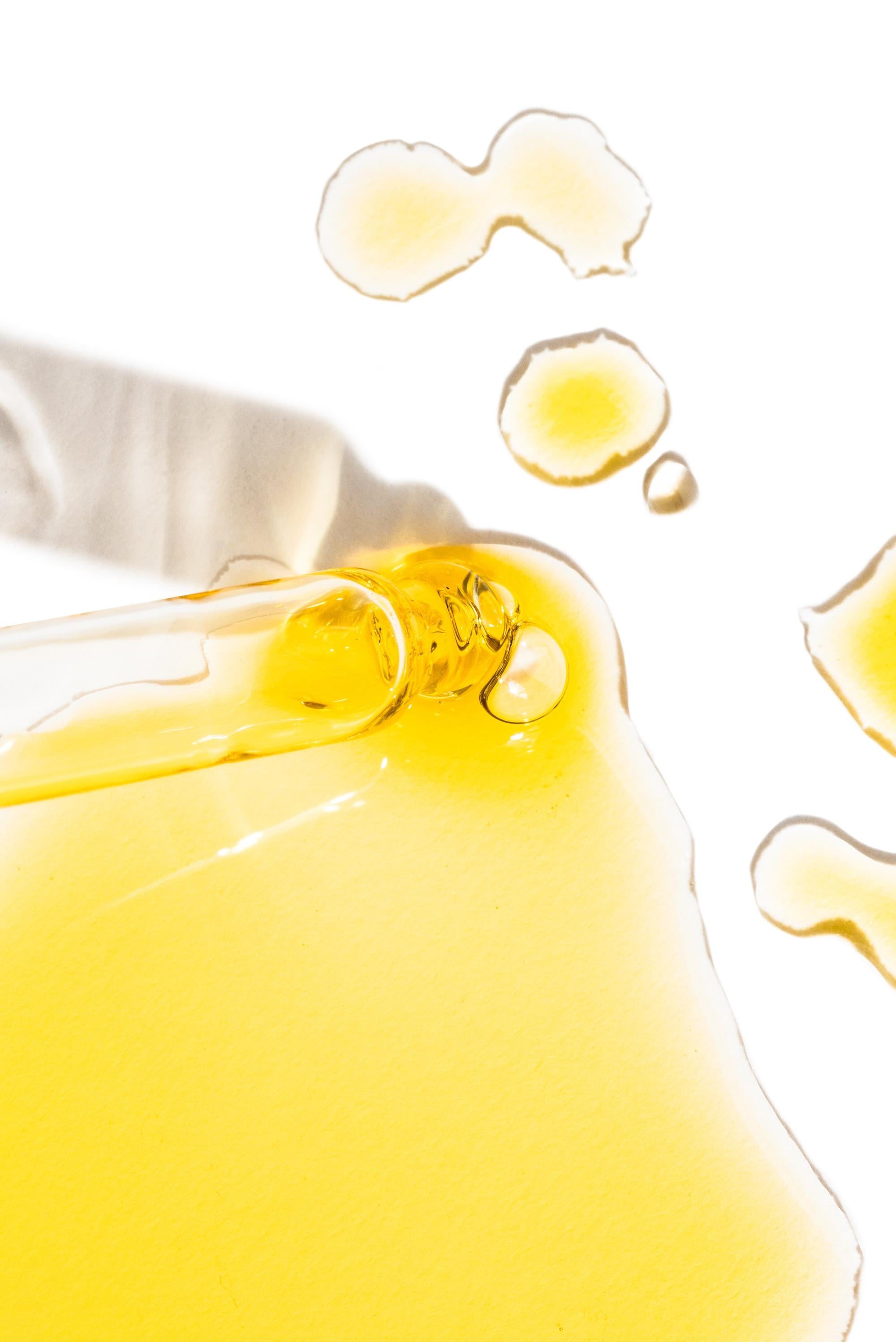 Close-up of golden Oxalis Apothecary Daily Glow Serum texture being applied with a glass dropper. The rich, lightweight botanical oil highlights the supercharged, hydrating formula for a natural skin glow.