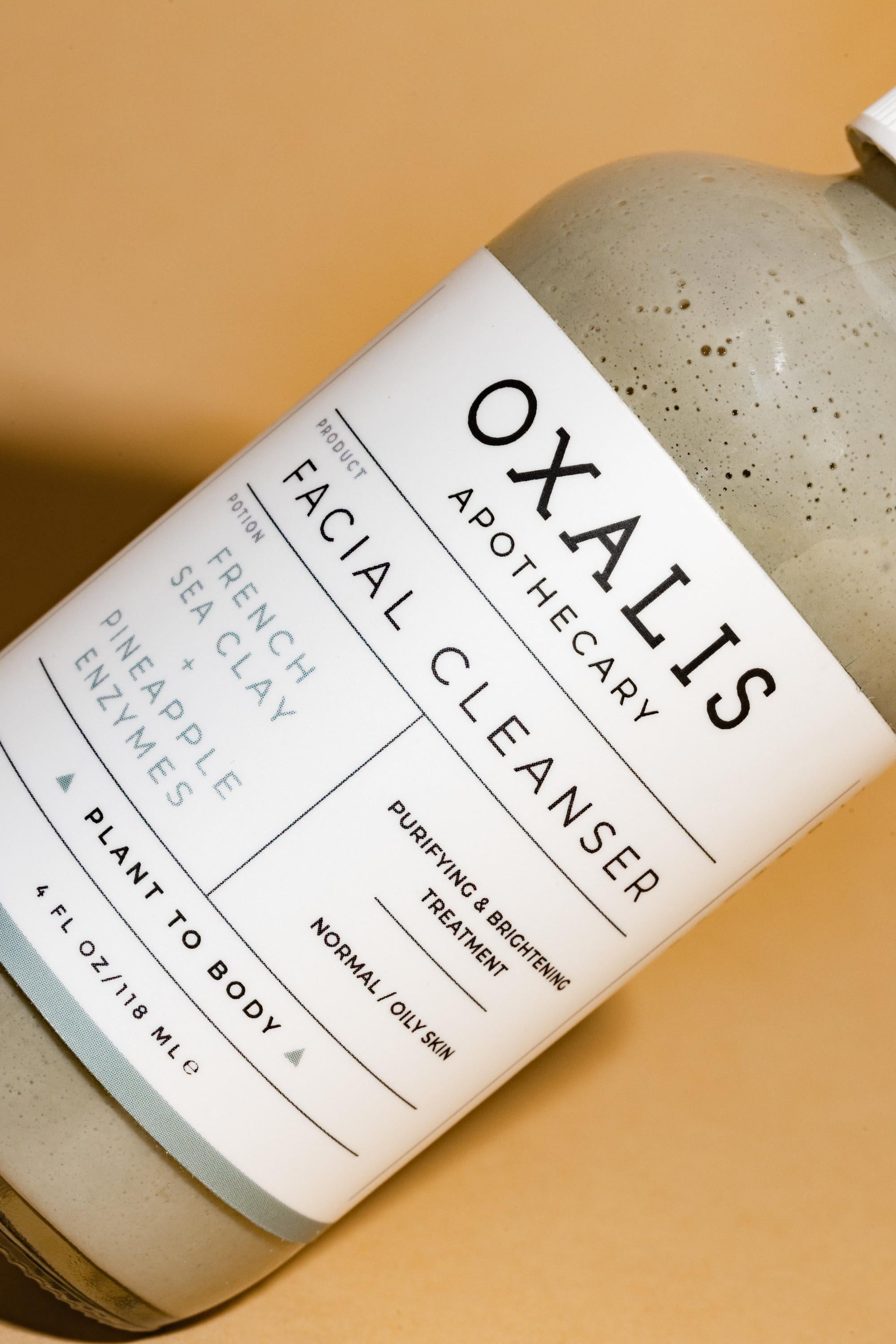 Oxalis Apothecary Facial Cleanser bottle showing purifying French Sea Clay and brightening Pineapple Enzyme ingredients.