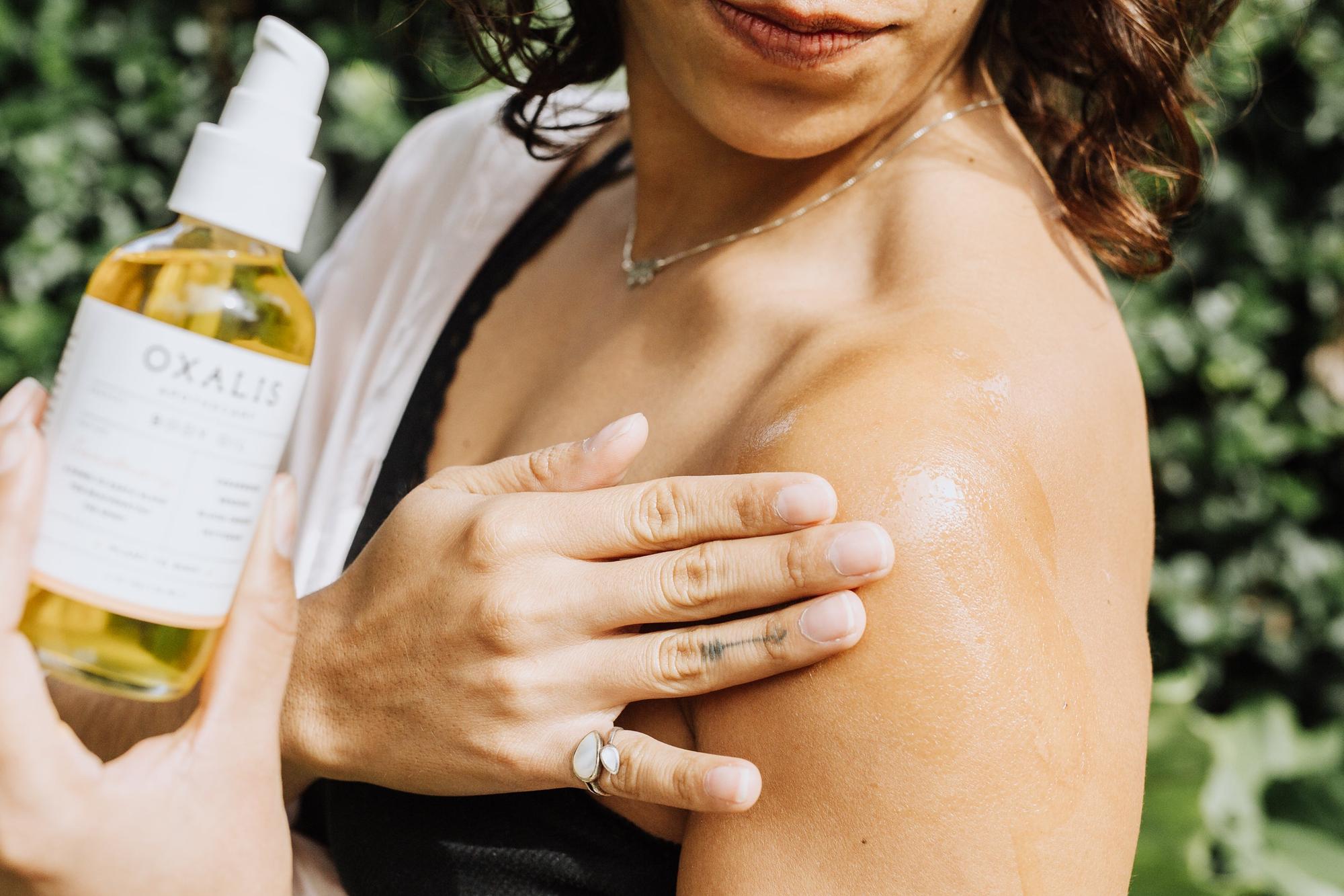 Close-up of a person applying Oxalis Apothecary Body Oil to their shoulder, demonstrating the hydrating glow and smooth texture of the woodsy botanical blend.